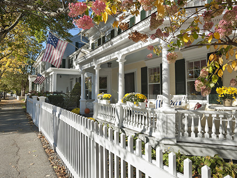 Side view of a white picket fence and home with a porch flying the Amercan flag