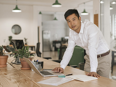 Asian man leaning on a desk with laptop