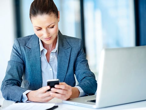 Businesswoman holding cellphone near laptop
