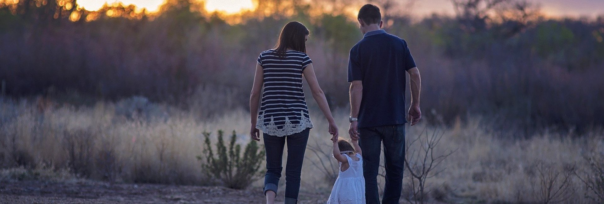 Dad, Mom and young girl walking toward a sunset